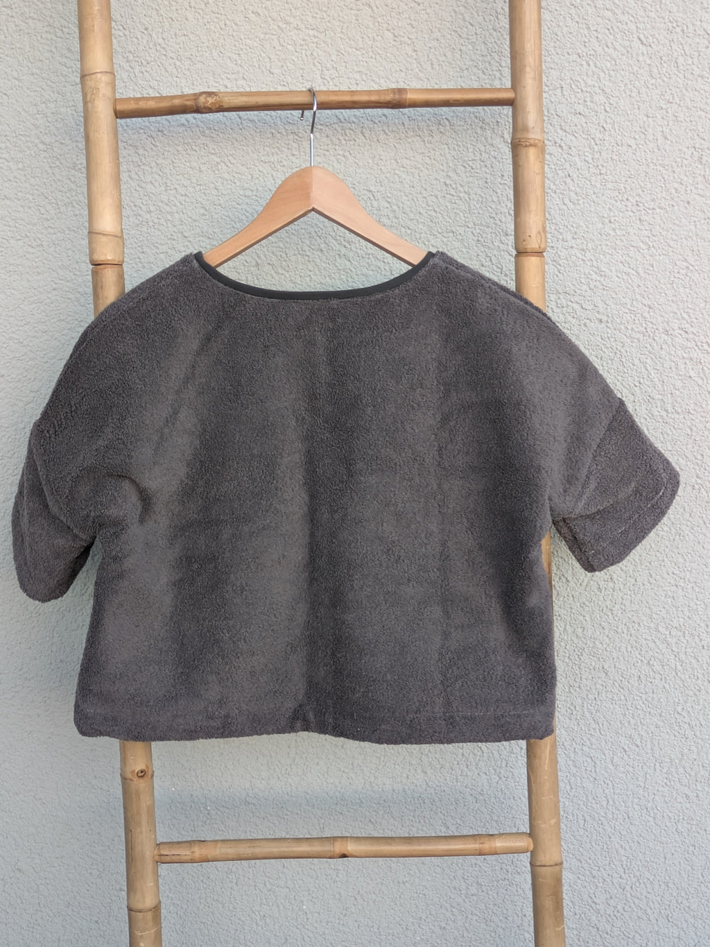 Rückansicht des dunkelgrauen Frottee Boxy Shirts 'Anthracite Wave ’71' von Old Wave. Zeigt den weiten Schnitt und die mittlere Naht. Das Shirt hängt an einem Holzkleiderbügel vor einer hellen Wand.