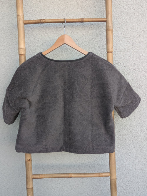 Rückansicht des dunkelgrauen Frottee Boxy Shirts 'Anthracite Wave ’71' von Old Wave. Zeigt den weiten Schnitt und die mittlere Naht. Das Shirt hängt an einem Holzkleiderbügel vor einer hellen Wand.