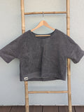 Vorderansicht des unifarbenen Frottee Boxy Shirts 'Anthracite Wave ’71' von Old Wave in Dunkelgrau. Mit Old Wave Logo-Patch unten links. Das Oberteil hängt auf einem Holzkleiderbügel an einer Bambusleiter.