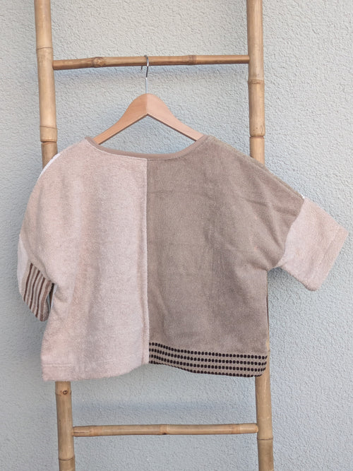 Rückansicht des Boxy Shirts 'Beige Coast ’70' von Old Wave im Half-and-Half-Look. Zeigt zwei unterschiedliche Beigetöne auf der linken und rechten Seite. Das Shirt hängt an einem Holzkleiderbügel vor einer hellen Wand.