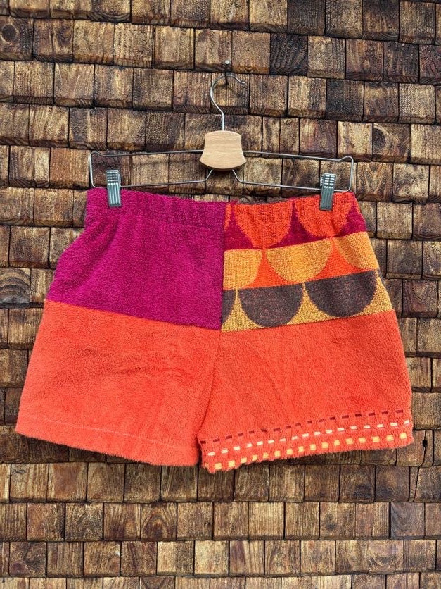 Rückansicht der Frottee-Shorts 'Blueberry' von Old Wave im farbenfrohen Patchwork-Design mit Magentapink, Knallorange, fächerförmigem 70s-Retro-Muster in Braun und Orange sowie einer Punkte-Bordüre am Saum.
