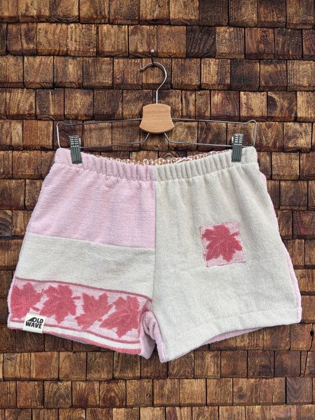 Vorderansicht der Frottee-Shorts 'Rose-Shell' von Old Wave im zweifarbigen Patchwork-Design in Rosa und Weiß mit altrosafarbener Ahornblatt-Bordüre am Saum, einzelnem Ahornblatt-Patch und Old Wave Logo unten links.