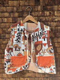 Vorderansicht der wendbaren Frottee-Weste 'Clementine' von Old Wave. Ärmellose Weste mit auffälligem 70s-Retro-Print in Orange, Braun, Schwarz und Cremeweiß sowie zwei orangefarbenen aufgesetzten Taschen vor einer Backsteinwand.