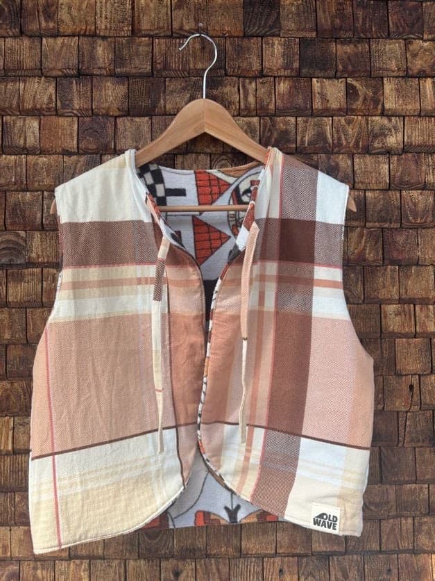 Vorderansicht der gewendeten Frottee-Weste 'Clementine' von Old Wave. Zweite Trageoption mit großflächigem Karomuster in warmem Orange, Rostbraun und Beige vor einer Backsteinwand.