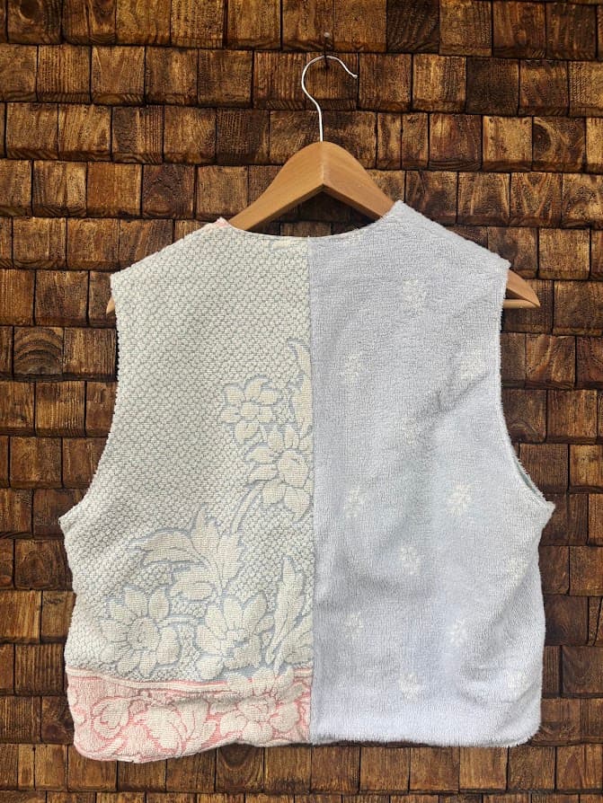 Rückansicht der Frottee-Weste 'Cloud Reversible ’72' von Old Wave. Zeigt die zweigeteilte blau-weiße Rückseite mit dezentem Musterfrottee und leichtem Rosa-Akzent am Saum vor einer Backsteinwand.