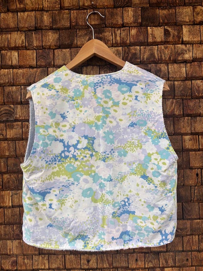 Rückansicht der gewendeten Frottee-Weste 'Cloud Reversible ’72' von Old Wave. Zeigt das durchgehende, farbenfrohe Retro-Aquarellmuster auf der Rückseite vor einer Backsteinwand.