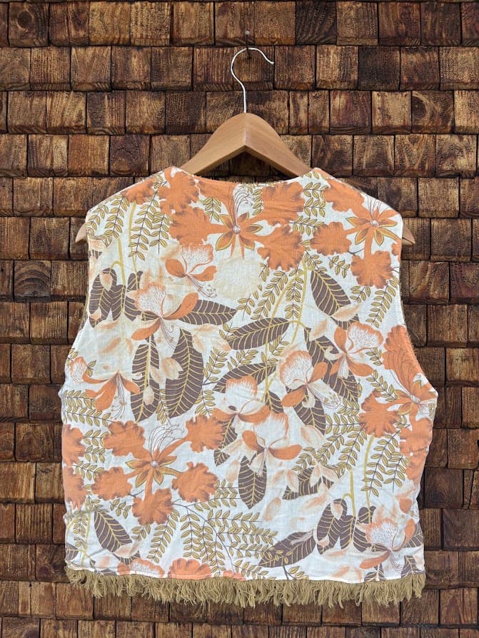 Rückansicht der gewendeten Frottee-Weste 'Dune' von Old Wave. Zeigt das durchgehende, florale Retromuster in Terracotta und Orange auf der Rückseite vor einer Backsteinwand.