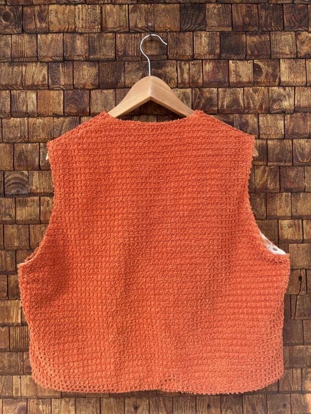 Rückansicht der Frottee-Weste 'Rust' von Old Wave. Zeigt die unifarbene, strukturierte Rückseite aus rostorangenem Frotteestoff vor einer Backsteinwand.