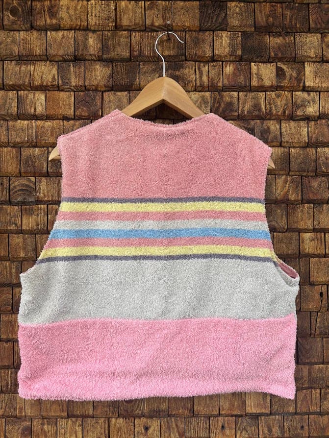 Rückansicht der Frottee-Weste 'Sienna' von Old Wave. Zeigt das dreifarbige Design mit grauer Mitte, bunten Akzentstreifen und rosa Saum vor einer Backsteinwand.