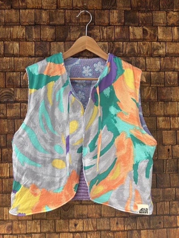 Vorderansicht der gewendeten Frottee-Weste 'Violet' von Old Wave. Zweite Trageoption in Flieder und Violett mit feinem floralen Ornamentmuster und Paisley-Details vor einer Backsteinwand.