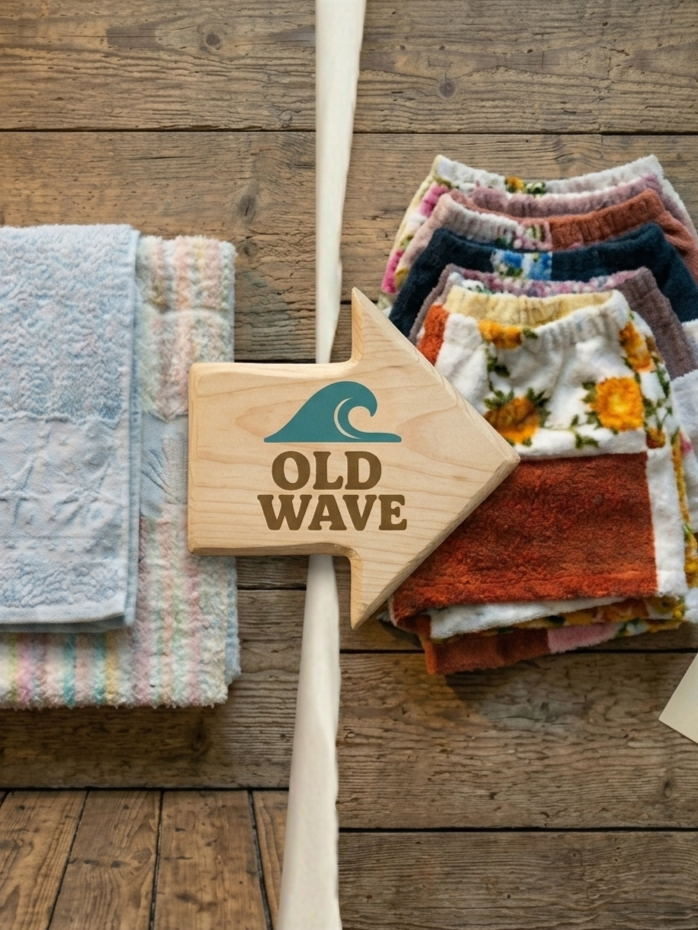 Links liegen zusammengelegte Vintage-Handtücher, in der Mitte zeigt ein Holzpfeil mit dem türkisen Old Wave Wellen-Logo nach rechts auf einen Stapel fertiger Upcycling-Shorts aus bunten Frottee-Handtüchern.