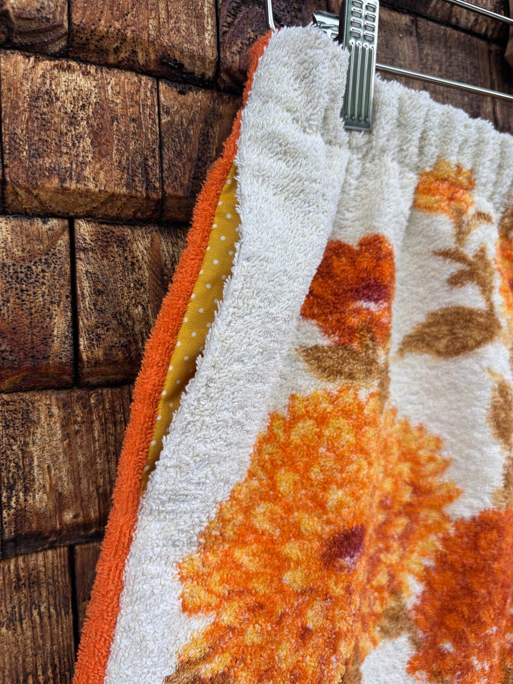 Nahaufnahme der seitlichen Tasche und der aufwendig verarbeiteten Seitennaht der „Autumn Bloom ‘72“ Frotteeshorts von Old Wave. Der Fokus liegt auf dem harmonischen Mustermix aus dem weißen Vintage-Stoff mit orange-braunen Blumen und den farbenfrohen Patchwork-Einsätzen in Gelb und Orange am Tascheneingriff.