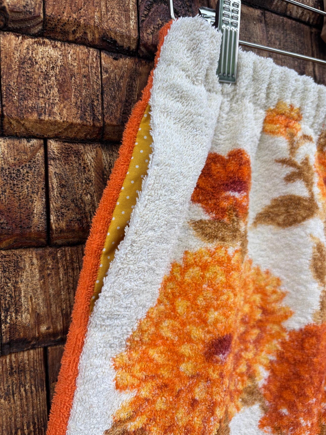 Nahaufnahme der seitlichen Tasche und der aufwendig verarbeiteten Seitennaht der „Autumn Bloom ‘72“ Frotteeshorts von Old Wave. Der Fokus liegt auf dem harmonischen Mustermix aus dem weißen Vintage-Stoff mit orange-braunen Blumen und den farbenfrohen Patchwork-Einsätzen in Gelb und Orange am Tascheneingriff.