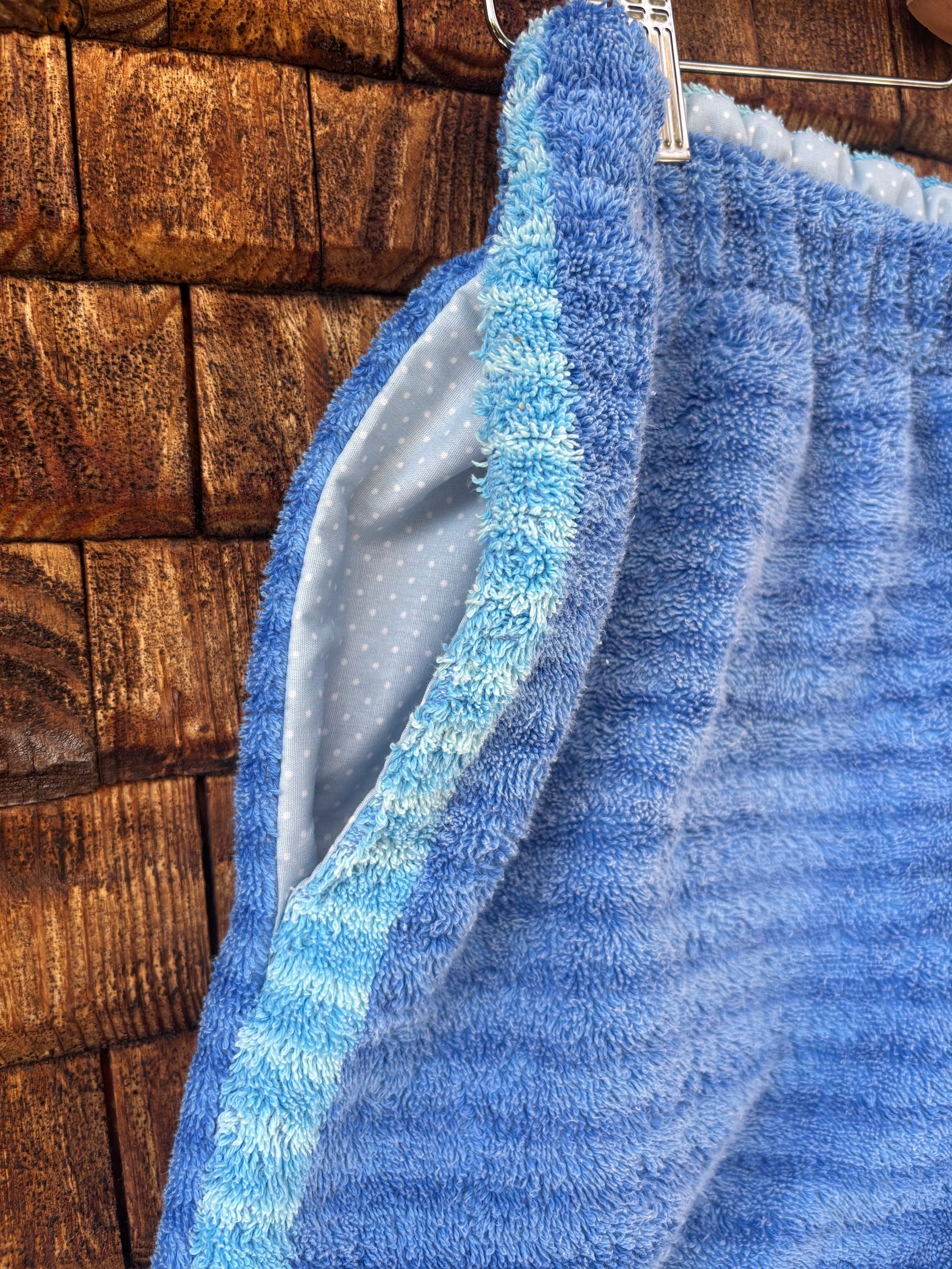 Nahaufnahme der seitlichen Eingriffstasche der Upcycling-Frotteeshorts „Deep Ocean ‘88“ von Old Wave. Das Detail zeigt die saubere Nahtführung und das graue Innenfutter der Tasche, die harmonisch in das dunkelblau gestreifte Frottee eingelassen ist, akzentuiert von einem hellblau-türkis gestreiften Bortenstreifen entlang des Tascheneingriffs.