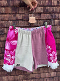 Upcycling-Shorts „Flamingo '74“ von Old Wave auf einem Kleiderbügel vor einer hellen, weißen Zimmertür. Das asymmetrische Patchwork-Design besteht aus upgecycelten Frottee-Handtüchern. Die linke Vorderseite zeigt im oberen Bereich ein markantes, leuchtend blaues Retro-Fliesenmuster mit weißen Ornamenten, das an eine hellgrau melierte Grundfläche grenzt. Das rechte Hosenbein ist vorwiegend in Hellgrau gehalten und schließt an der Außenkante mit einem vertikalen Streifen des blauen Mustermaterials ab.