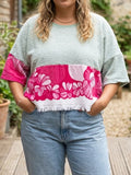 Nahaufnahme eines Models, das das Upcycling-Towel Boxy Shirt „Lemon '65“ von Old Wave in Größe L trägt. Das lockere, mintgrüne Frottee-Oberteil zeigt im unteren Bereich ein auffälliges, pink-weißes Retro-Blumenmuster, das mit Fransen am Saum abschließt. Kombiniert wird das nachhaltige Oversize-Shirt mit einer hellblauen Jeans.