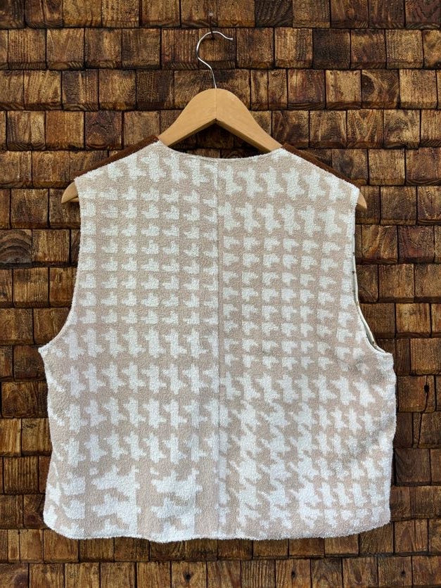 Rückansicht der gewendeten Frotteeweste 'Biscuit' von Old Wave. Zeigt ein feines, beigefarbenes Hahnentritt-Muster im Patchwork-Look vor einer dunklen Holzziegel-Wand.