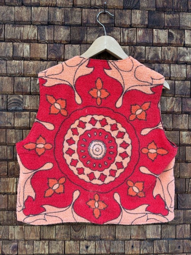Rückansicht der Frottee-Wendeweste 'Daisy' von Old Wave. Zeigt das große, kreisförmige Mandala-Blütenmotiv in Knallrot und Orange auf einem Kleiderbügel.