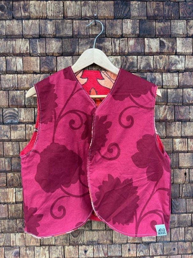 Vorderansicht der gewendeten Frotteeweste 'Daisy' von Old Wave in leuchtendem Magenta mit dunkelrotem Ranken- und Blättermuster auf einem Holzkleiderbügel.