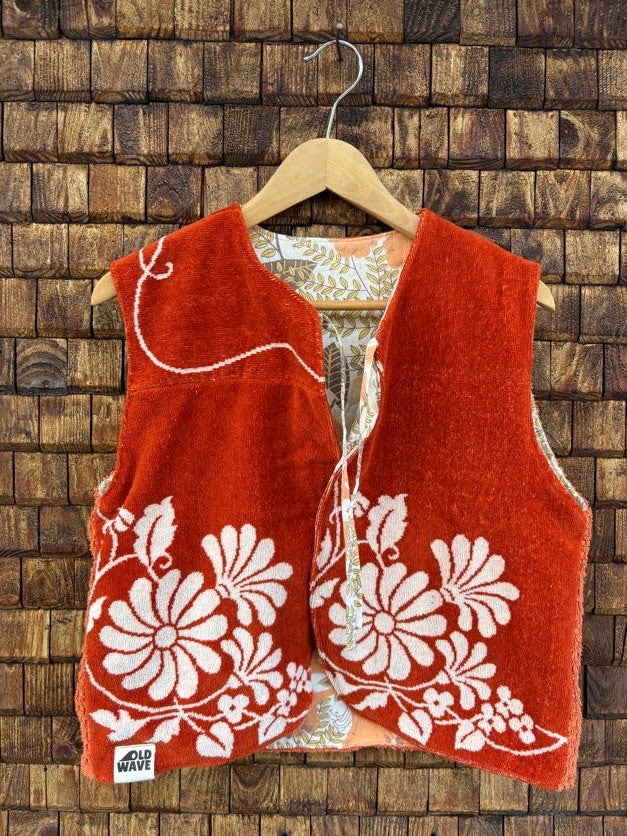 Vorderansicht der gewendeten Frotteeweste 'Laguna' von Old Wave in kräftigem Terrakotta-Orange mit weißer Retro-Blumenbordüre am unterem Saum und Logo-Patch unten links.