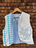 Vorderansicht der gewendeten Frotteeweste 'Ocean' von Old Wave im Patchwork-Design mit blau-weißem Hahnentritt-Muster, weißem Frottee mit hellblauer Blumenstickerei und Logo-Patch unten links.