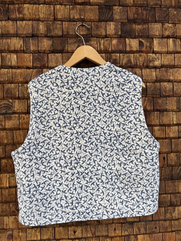 Rückansicht der gewendeten Weste 'Riviera' von Old Wave. Schlichte Ansicht im durchgehenden, feinen blau-weißen Vintage-Print vor einer dunklen Holzziegel-Wand.