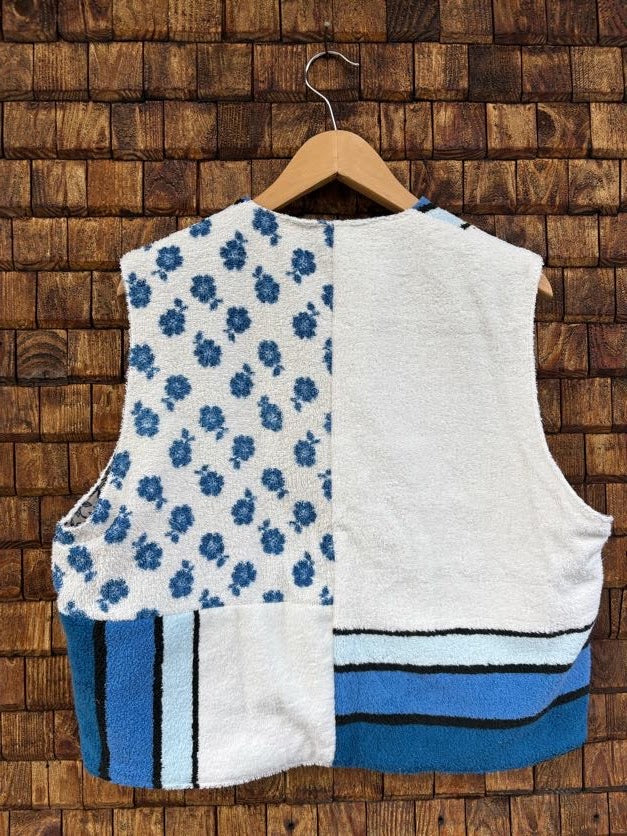 Rückansicht der Frottee-Wendeweste 'Riviera' von Old Wave. Zeigt das zweigeteilte Patchwork-Design mit blauem Blättermuster oben links, weißem Frottee rechts sowie Querstreifen-Details am unteren Saum.