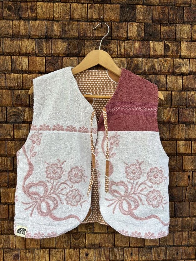 Vorderansicht der gewendeten Frotteeweste 'Rose-Shell' von Old Wave im Patchwork-Look aus weißem Frottee mit altrosafarbener Blumenstickerei, dunkelrotem Schulterelement und Bindebändern.