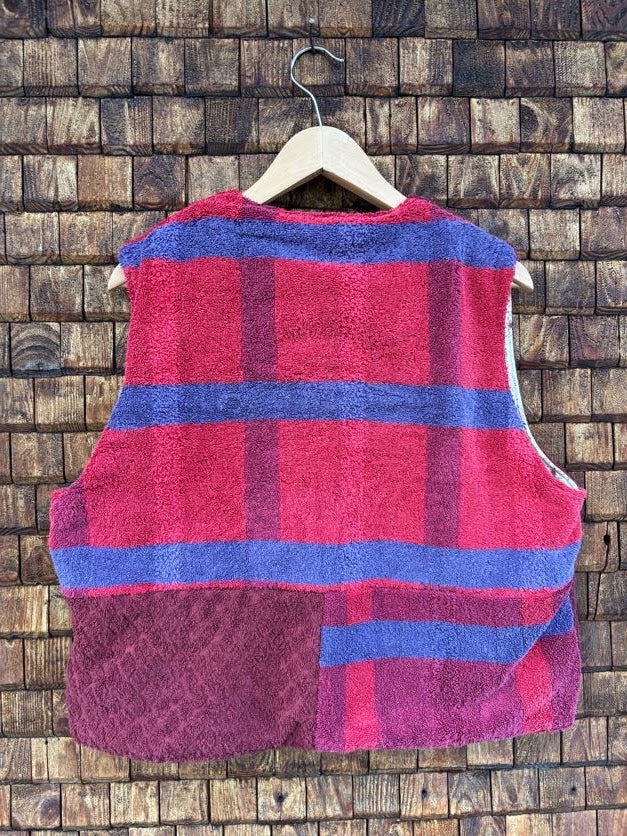 Rückansicht der gewendeten Weste 'Sol' von Old Wave mit großem Karomuster in Rot, Magenta und Blau im Retrostil vor einer Holzziegel-Wand.