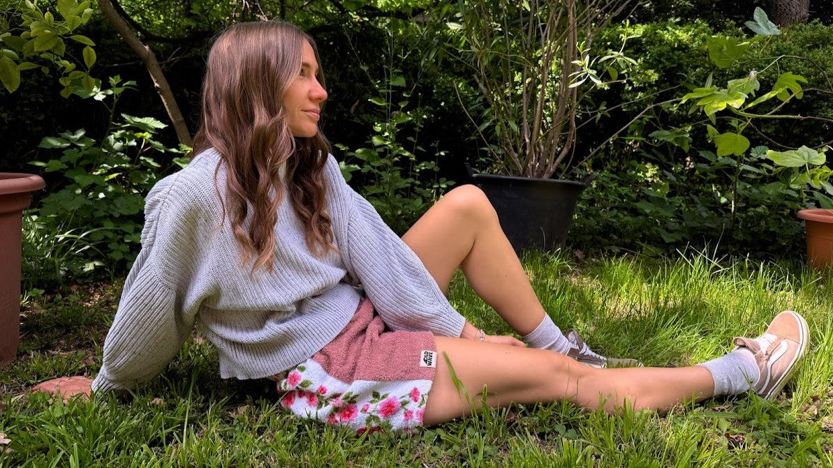 Model sitzt im Garten und trägt eine handgefertigte Old Wave Upcycling-Shorts aus einer Kombination aus rosa Frottee-Handtuch und Vintage-Stoff mit Rosen-Muster.
