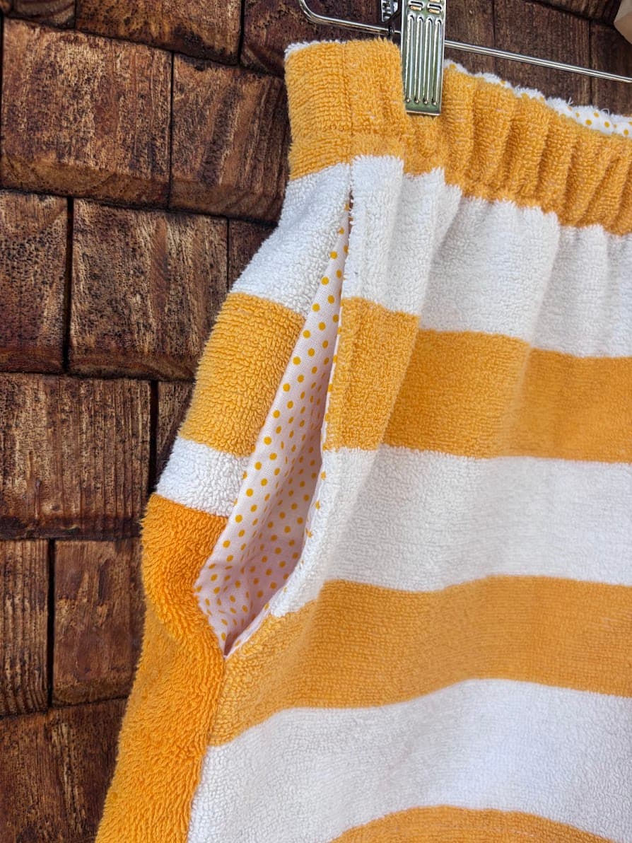 Detailaufnahme der seitlichen Eingriffstasche der handgefertigten Sunstripe ‘79 Shorts, die ein feines, weißes Futter, im Kontrast zu den orange-weißen Frottee-Streifen zeigt.
