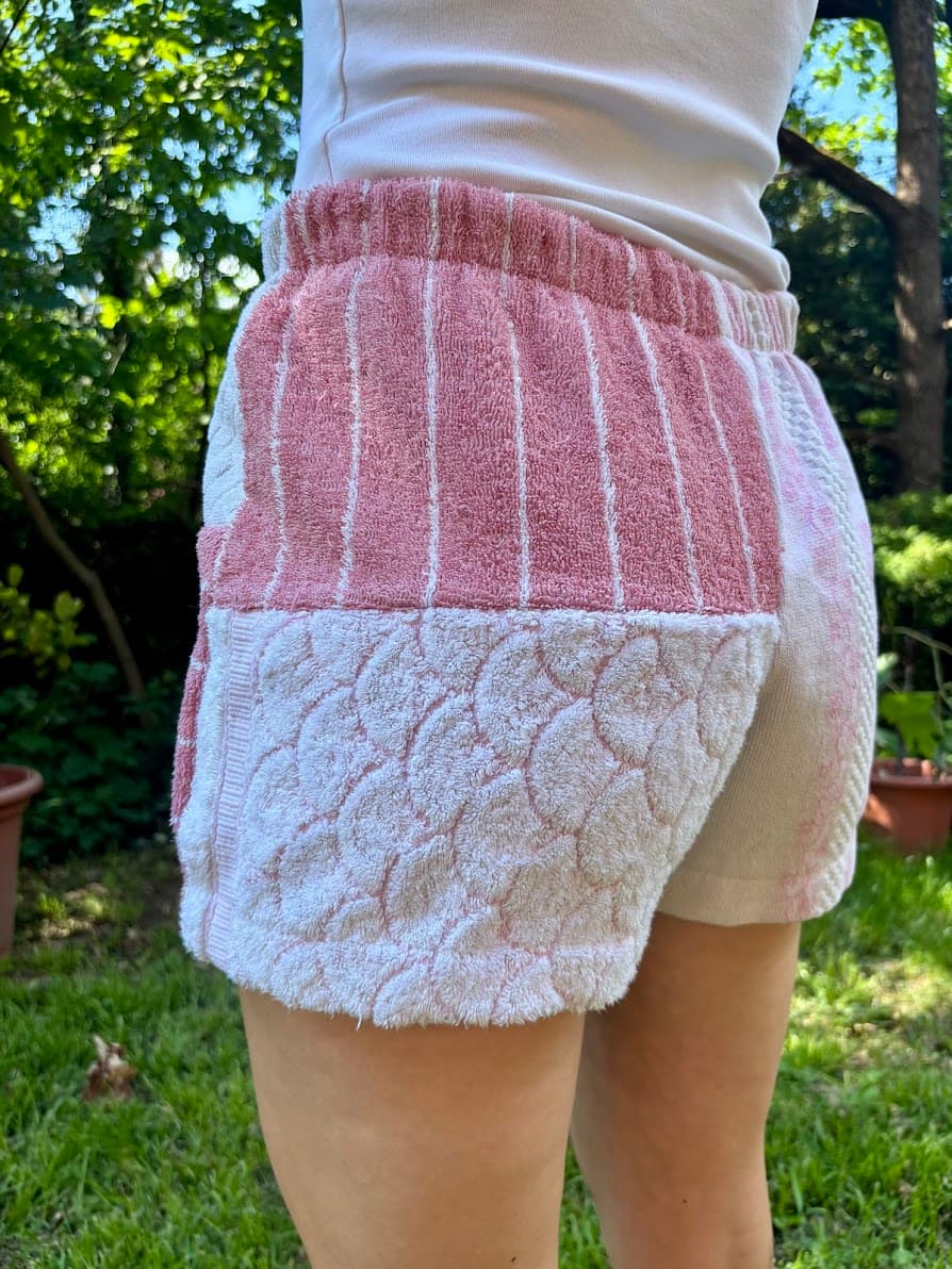 Getragene Rückansicht, schräg nach rechts gedreht. Im Fokus steht ein wunderschönes, plastisch eingewebtes Schuppen- oder Wellenmuster in Weiß auf der unteren Gesäßhälfte, kombiniert mit rosa-weiß gestreiftem Frottee am Bund.