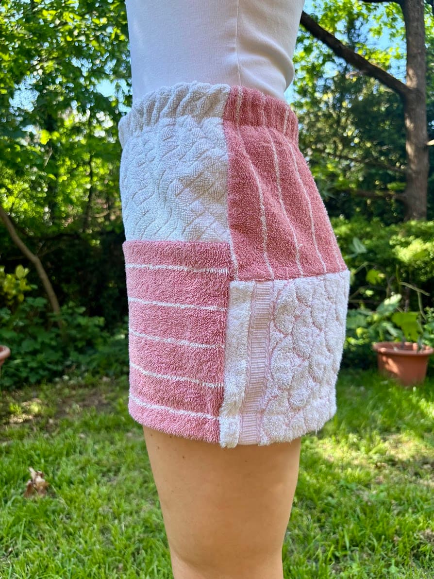 Getragene Seitenansicht von rechts. Das Bein zeigt vertikal verlaufende Webstrukturen und Streifen in Rosa und Weiß. Am Saum ist der weiße Old Wave Logo-Patch eingenäht.