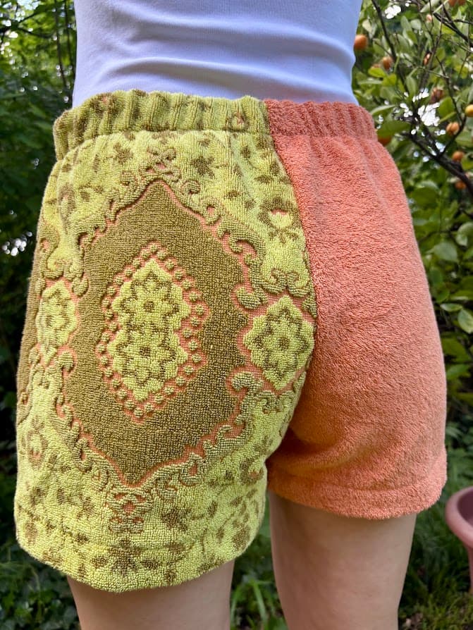 Getragene Rückansicht, leicht nach rechts gedreht. Im Fokus steht die gemusterte Gesäßseite im Retro-Look der 70er Jahre, die harmonisch in das unifarbene Orange des rechten Beins übergeht.