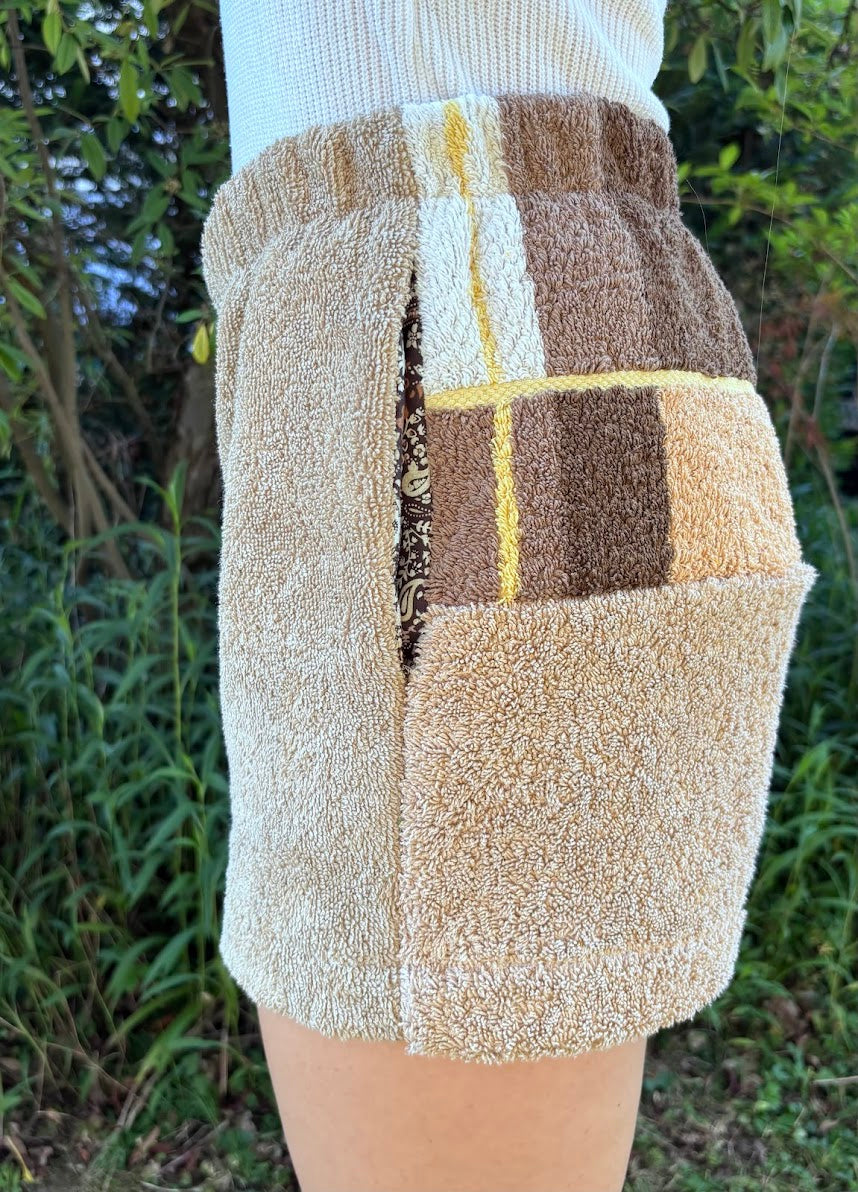 Seitliche Trageansicht der Shorts Meadow Campagna 68 mit Fokus auf das strukturierte Frottee-Patchwork in Braun und Sandtönen sowie die integrierte Seitentasche.