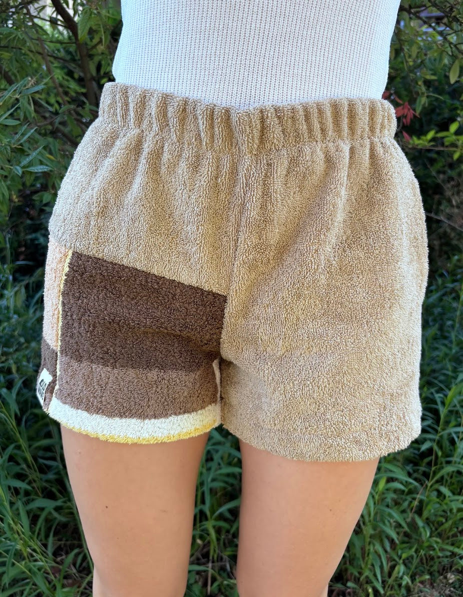 Vorderansicht der am Modell getragenen Frottee-Shorts Meadow Campagna 68 in der Natur. Die bequeme Passform mit elastischem Bund hebt das harmonische Design aus beigen und braunen Vintage-Stoffen hervor.