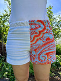 Vorderansicht der Frottee-Shorts Sardinia Summer 72 im lebendigen Patchwork-Look. Die rechte Hälfte zeigt ein auffälliges, korallenrotes Vintage-Paisleymuster mit hellblauen Akzenten, während die linke Hälfte aus weißem Struktur-Frottee mit zarten, hellblauen Längsstreifen besteht.