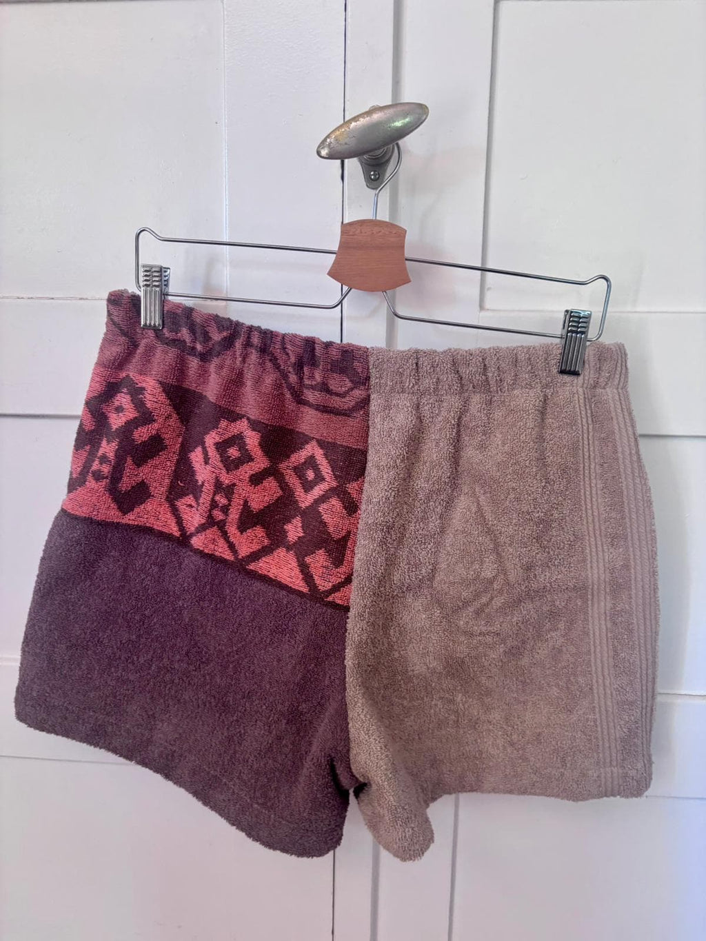 Rückansicht der auf einem Bügel hängenden Frottee-Shorts Siena Terra 75 vor hellem Hintergrund. Das Bild betont den bequemen, gerafften Elastikbund und die hochwertige Verarbeitung der verschiedenen weichen Vintage-Baumwollstoffe.