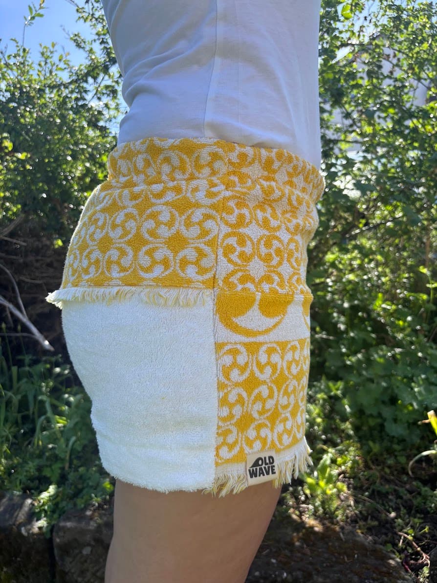 Rückansicht von schräg rechts der Vintage-Shorts vor grünem Garten-Hintergrund. Zu sehen ist die weiße Struktur der rechten Gesäßhälfte und der elastische, geraffte Bund, kombiniert mit dem gemusterten Seitenpanel.