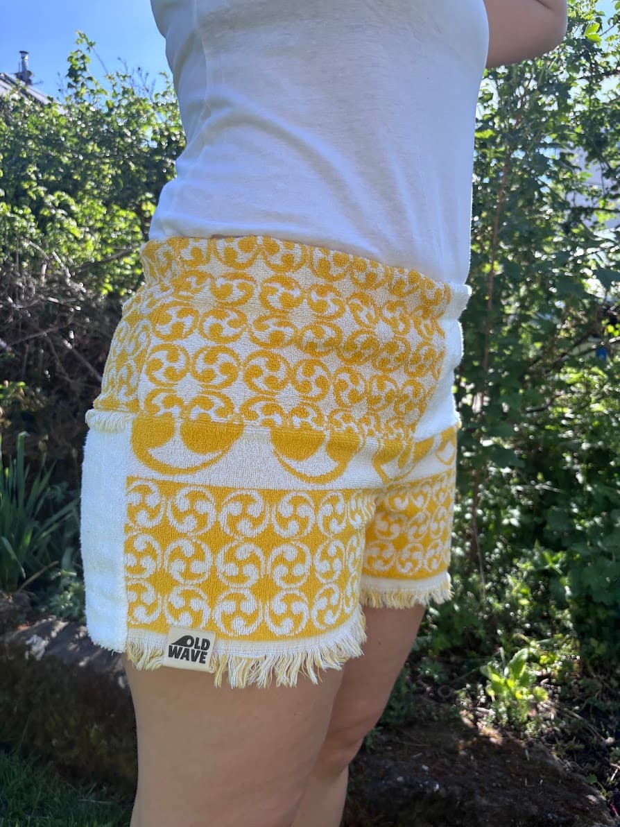 Seitliche Profil-Ansicht von rechts der Frottee-Shorts Sole di Capri 73. Das Hosenbein zeigt im unteren Bereich das detaillierte, gelbe Webmuster und schließt am Saum mit dem eingenähten, weißen Old Wave Logo-Patch ab.