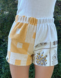 Vorderansicht der am Modell getragenen Frottee-Shorts Sunfade Twist 71 in einer grünen Außenumgebung. Der elastische Bund und der lockere Schnitt betonen den sommerlichen Retro-Look der verschiedenen Musterelemente.