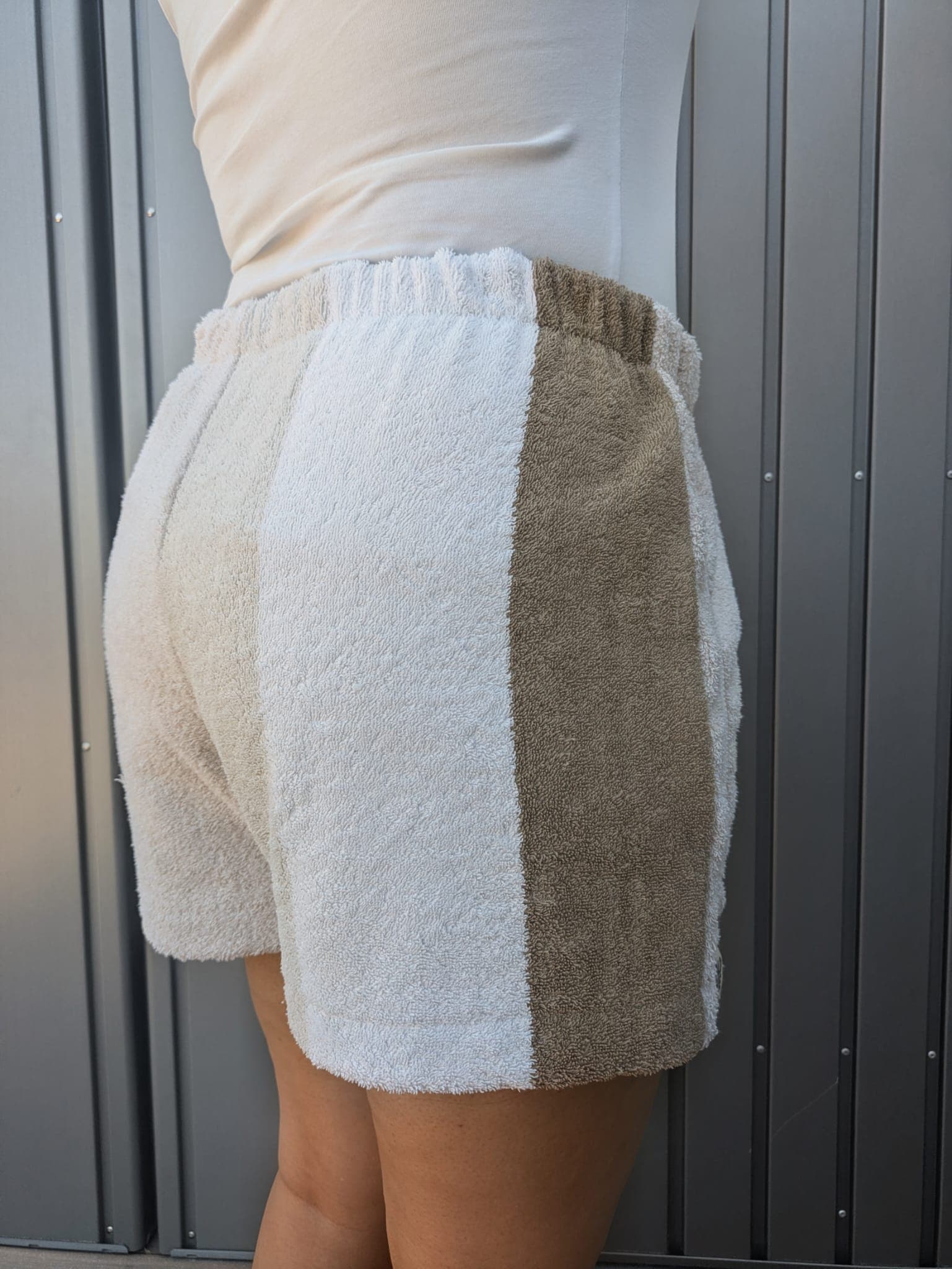 Rückansicht der Terra Breeze 79 Frottee-Hose, schräg nach links gedreht. Die Gesäßpartie spiegelt das asymmetrische Design wider: Die linke Seite ist komplett in schlichtem Weiß gehalten, die rechte Seite besticht durch das strukturierte Natur- und Sandbraun.