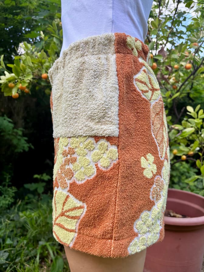 Nahaufnahme der rechten Seitenansicht. Im oberen Bereich am Bund ist das sandbeige Frottee-Inlay zu sehen, welches nach unten hin in das markante, terracottatönige florale Retro-Muster übergeht.