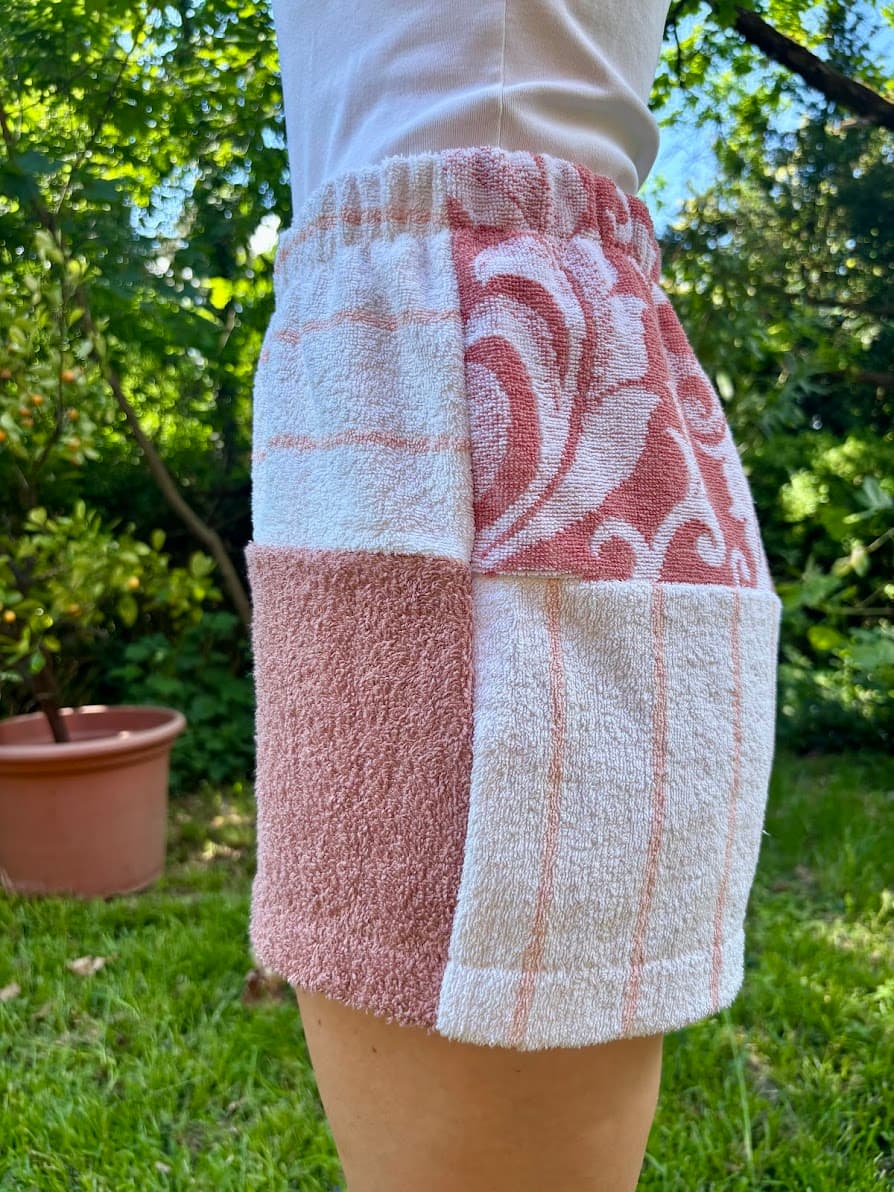 Getragene Seitenansicht von rechts. Das Bein zeigt eine dreigeteilte Struktur: Vorne das tiefe roséfarbene Barock-Ornamentmuster, in der Mitte ein unifarbenes siena-roséfarbenes Inlay und hinten ein weißes Frotteestück mit feinen Streifen.